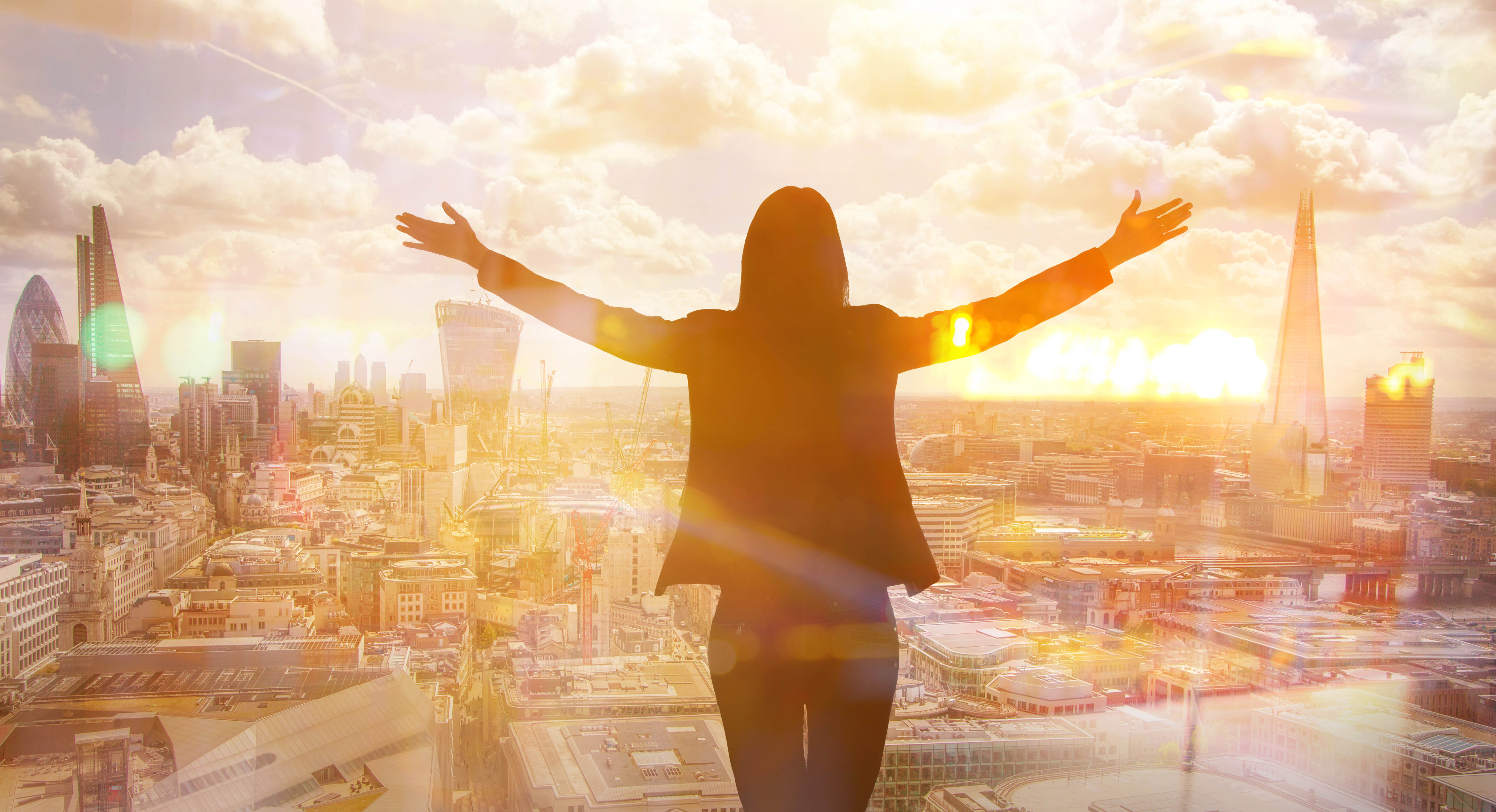 Woman standing with her arms raised, staring out at a city